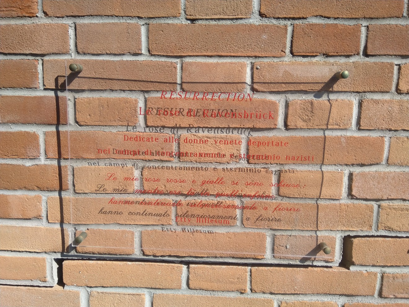 Targa commemorativa in vetro su muro di mattoni, dedicata alle donne deportate nei campi di concentramento.
