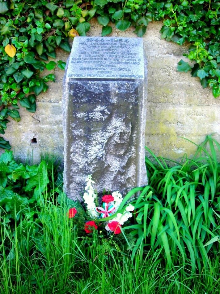 Cippo commemorativo immerso nella vegetazione, simbolo del decennale di un evento significativo.