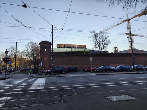 Pannelli informativi sul carcere Le Nuove, visibili da una strada con auto parcheggiate e il cantiere in background.