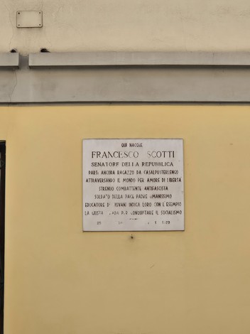 Lapide commemorativa di Francesco Scotti, senatore della repubblica, su muro giallo.