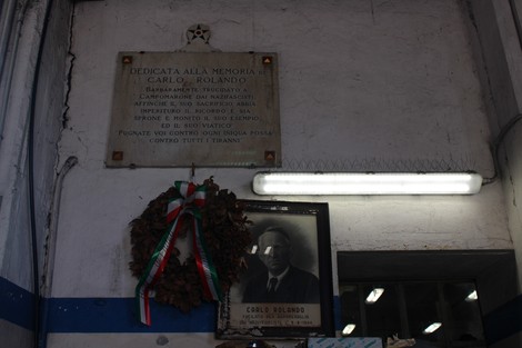 Lapide commemorativa dedicata a Carlo Rolando, con corona di fiori e un ritratto in bianco e nero.