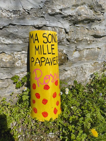 Monumento giallo decorato con scritte e fiori colorati, posizionato accanto a un muro di pietra.