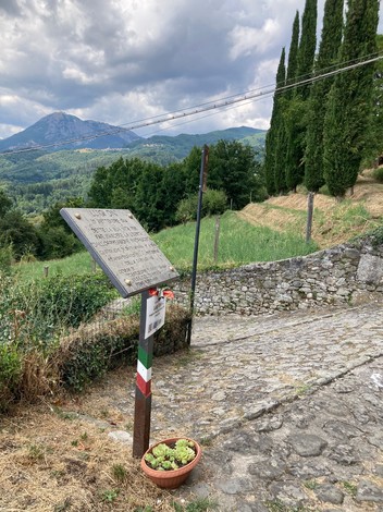 Lapide commemorativa immersa nel paesaggio montano, con vista su colline e alberi.
