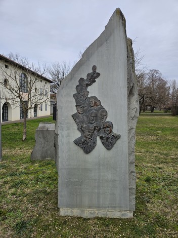 Monumento ai Partigiani, scultura commemorativa in pietra con volti di combattenti in un contesto verde e urbano.