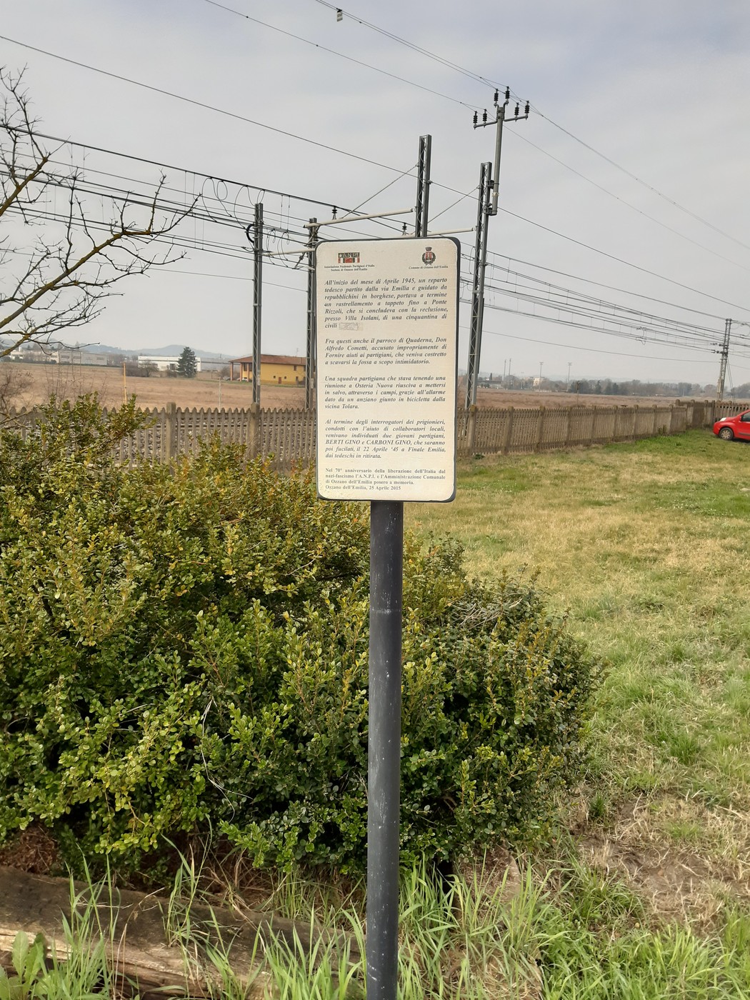 Targa informativa su un rastrellamento, situata in un'area aperta con vegetazione e linee elettriche sullo sfondo.