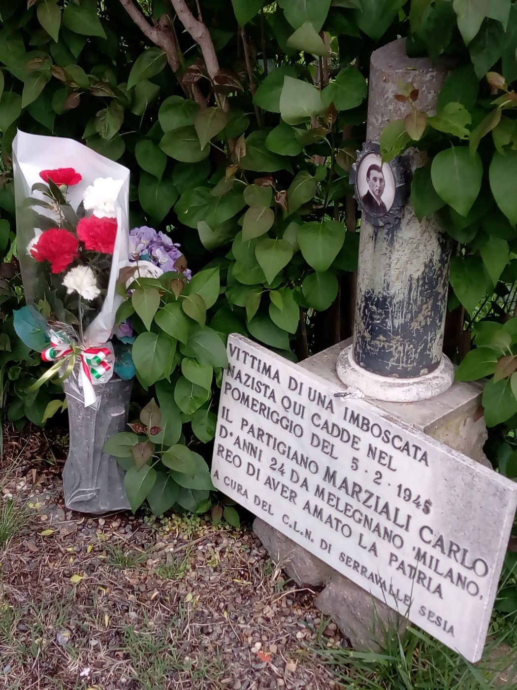 Cippo commemorativo per Carlo Marziali, vittima di un'imboscata nel 1948, con fiori e omaggio affettuoso.