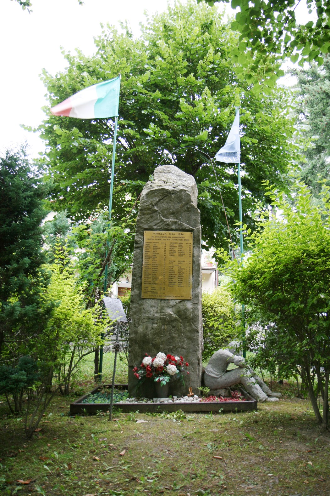 Monumento dedicato ai caduti del bombardamento, immerso nel verde, con bandiere e fiori a commemorare le vittime.