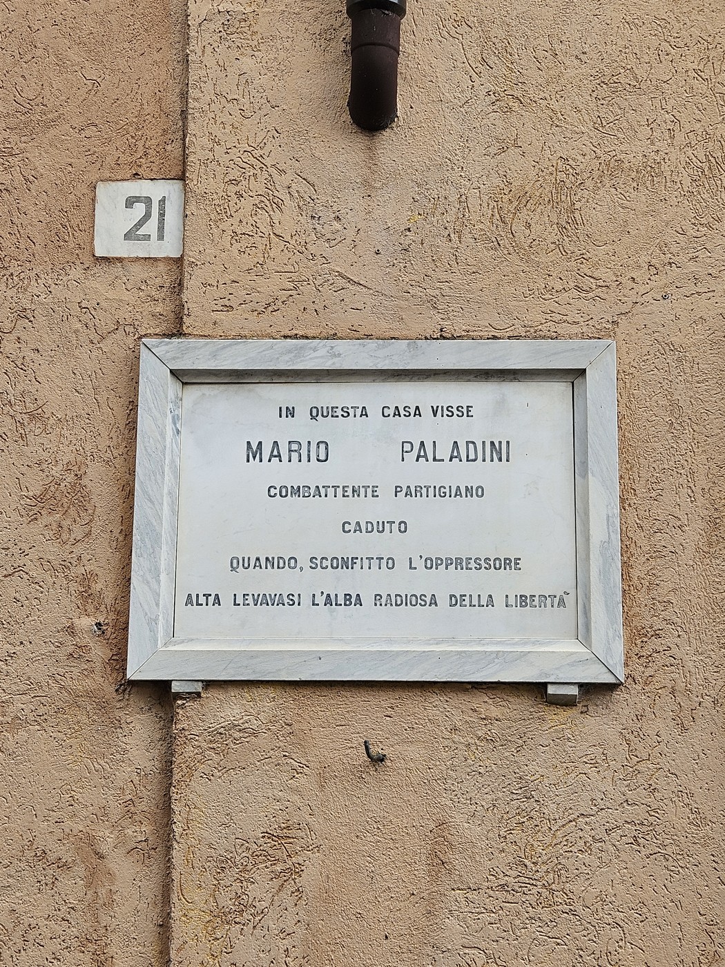 Lapide commemorativa di Mario Paladini, partigiano, situata su una parete esterna di un edificio.