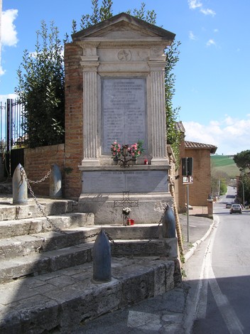 Tabernacolo ai caduti di Torrenieri, monumento commemorativo con decorazioni floreali e iscrizioni in un contesto rurale.