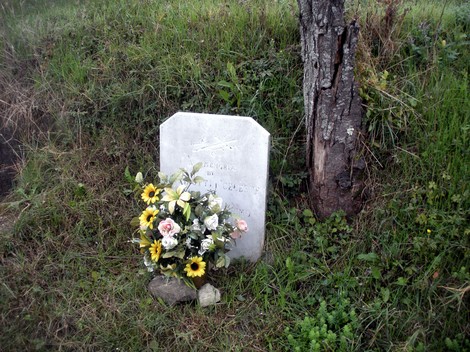 Cippo memoriale con fiori, situato in una zona verde, simbolo di ricordo e commemorazione.