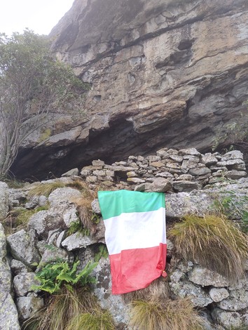 Rifugio partigiano "Non si trova" con bandiera italiana su un masso, circondato da rocce e vegetazione.