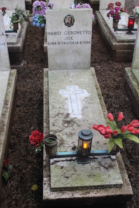 Tombe con fiori e candele, dedicate ai caduti per la Libertà. Atmosfera di rispetto e commemorazione.