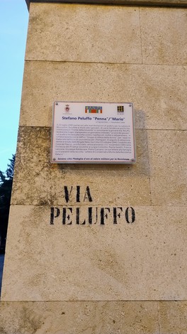 Targa informativa dedicata a Stefano Peluffo, con iscrizioni su una parete in pietra.