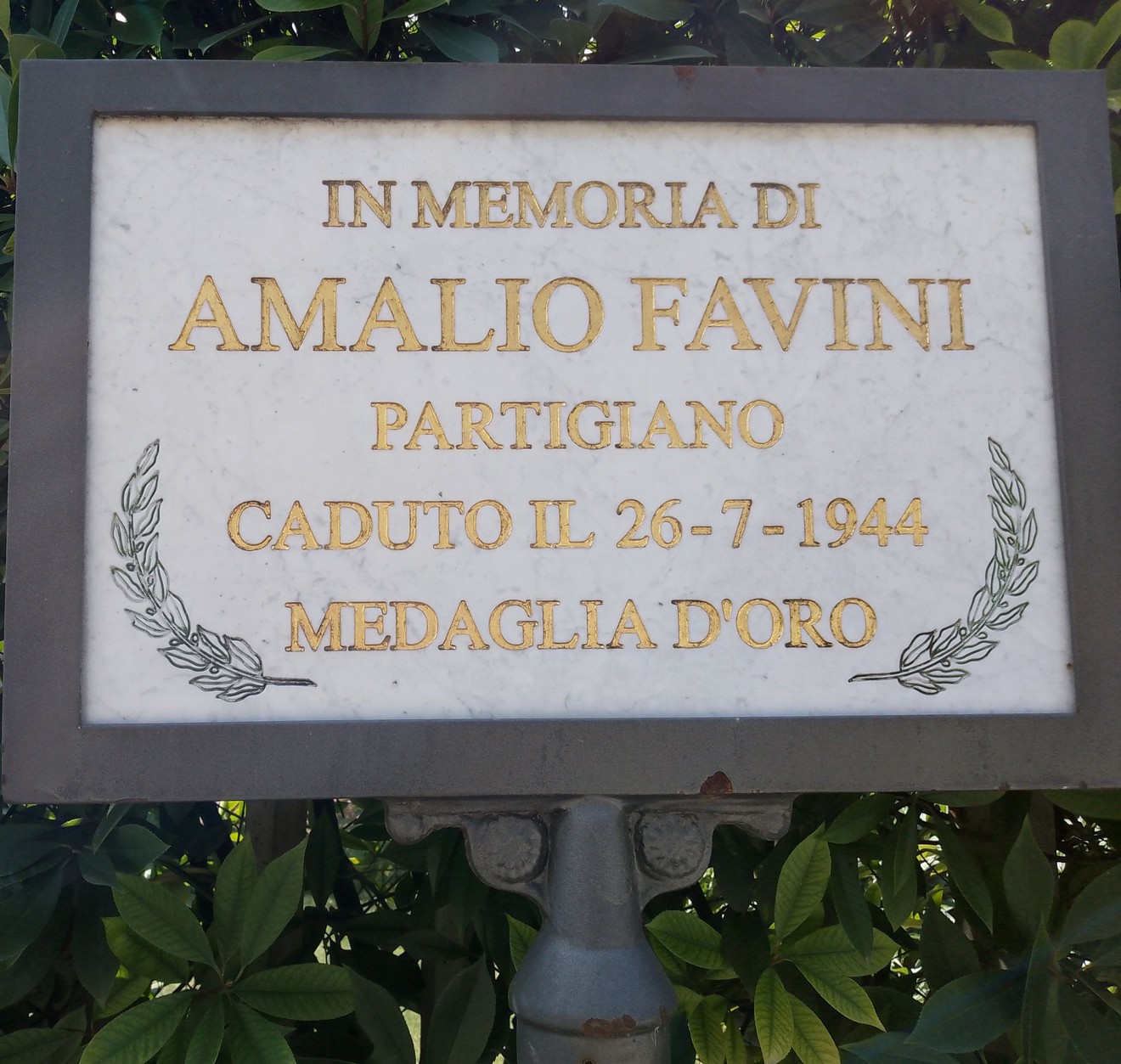 Lapide commemorativa di Amalio Favini, partigiano caduto nel 1944, con decorazioni artistiche e scritte dorate.
