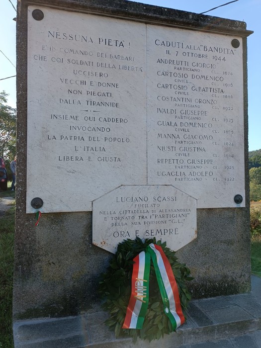 Lapide commemorativa dedicata ai caduti della Bandita di Cassinelle, con omaggio floreale e scritte di memoria storica.
