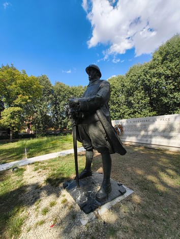 Monumento ai Caduti con soldato in uniforme, circondato da verde e cielo blu, simbolo di commemorazione e pace.