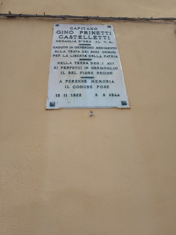 Lapide commemorativa dedicata a Gino Prinetti Castelletti, con riferimento alla sua medaglia d'oro e al sacrificio per la patria.