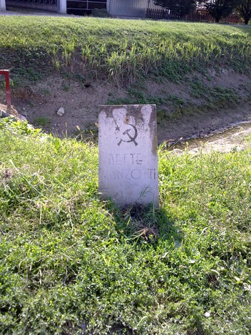 Cippo commemorativo dedicato a Manzotti, situato in un'area verde lungo un corso d'acqua.