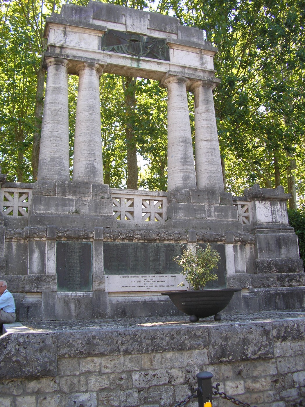 Monumento ai caduti con colonne e basamento, immerso in un contesto di verde. Rappresenta la memoria storica.