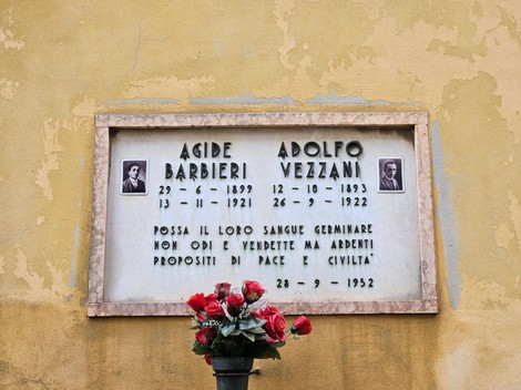 Lapide commemorativa dedicata a Agide Barbieri e Adolfo Vezzani, con decorazione floreale e cornice in pietra.