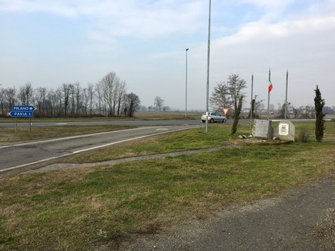 Monumento dell'eccidio sulla Vigentina, con bandiere italiane, in un paesaggio rurale.