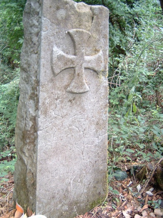 Cippo di Coperzano, un'antica stele in pietra con una croce, immersa nella natura.
