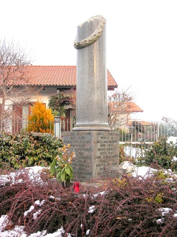 Cippo commemorativo ai caduti di Vaglio, circondato da fiori e ricordi in un paesaggio innevato.