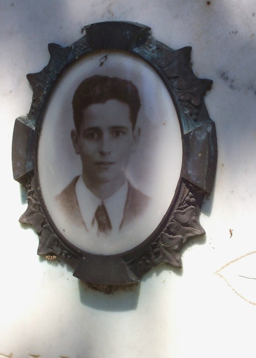 Ritratto vintage incorniciato di un giovane su sepolcro, caratterizzato da eleganza e ricordi familiari.