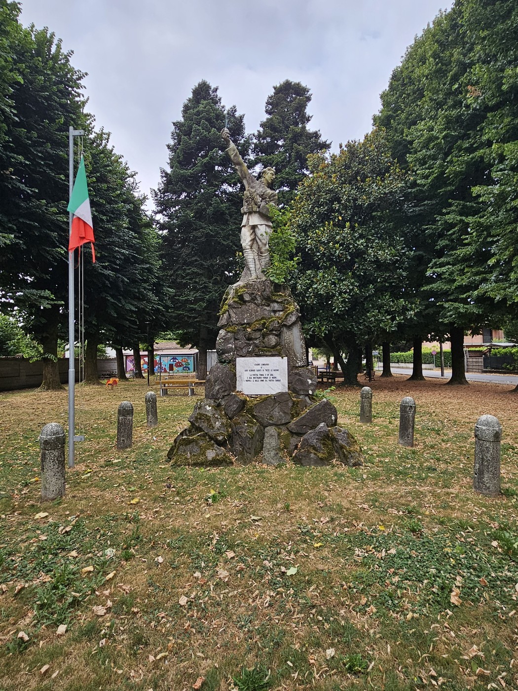 Monumento ai Caduti di Stagno Lombardo, circondato da alberi e cimeli, con una statua che commemora i caduti.