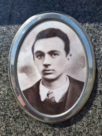 Ritratto in bianco e nero di un giovane uomo, inserito in una cornice ovale, su uno sfondo scuro.