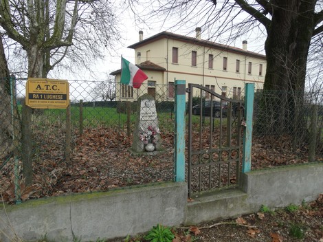 Cippo commemorativo a Pristanskov, circondato da un recinto e alberi, con bandiera italiana.