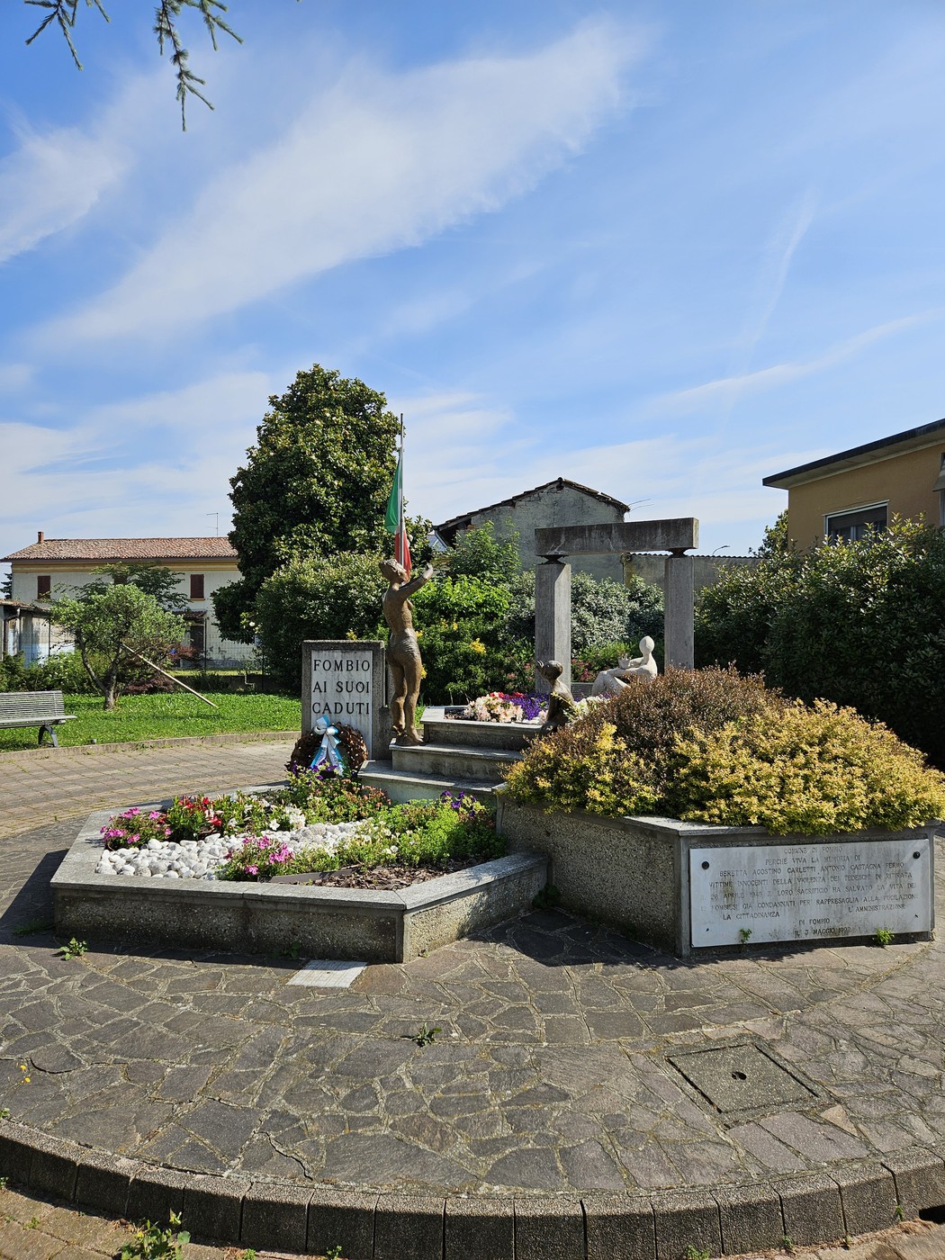 Monumento commemorativo con statue, fiori e bandiera, dedicato a Beretta, Carletti e Castagna in un parco.