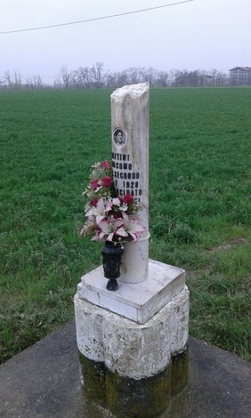 Cippo a Pattini: monumento commemorativo con fiori, immerso in un campo verde.