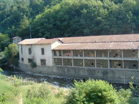 Lapide del Lanificio Tronci: edificio storico industriale situato lungo un corso d'acqua, circondato da verde.