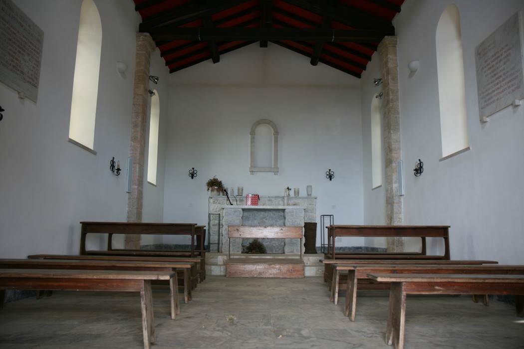 Interno della Chiesetta dei Partigiani del Pasquilio, con panche in legno e pareti semplici e luminose.