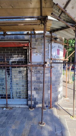 Targa di un bar con impalcatura in primo piano, situata in un'area urbana.