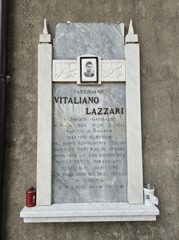 Lapide dedicata a Vitaliano Lazzari, partigiano caduto nel 1945, adornata da una fotografia e candele commemorative.