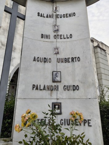 Monumento con fotografie e nomi dei deportati, circondato da fiori, in memoria delle vittime.