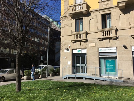 Lapide commemorativa su un edificio, in un contesto urbano con vegetazione e viabilità.