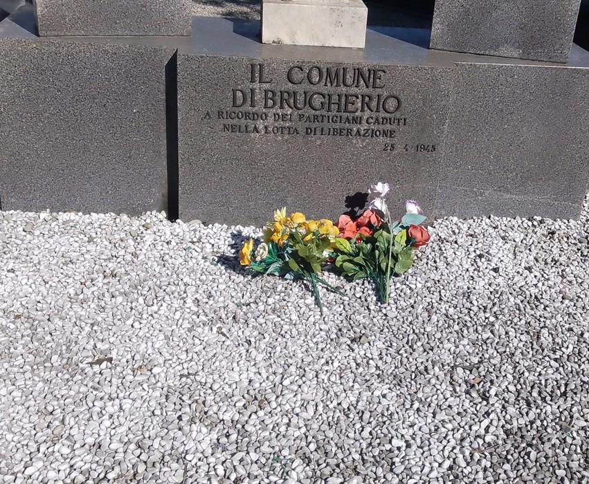 Monumento commemorativo ai partigiani caduti, con fiori colorati e pietre bianche sul terreno circostante.