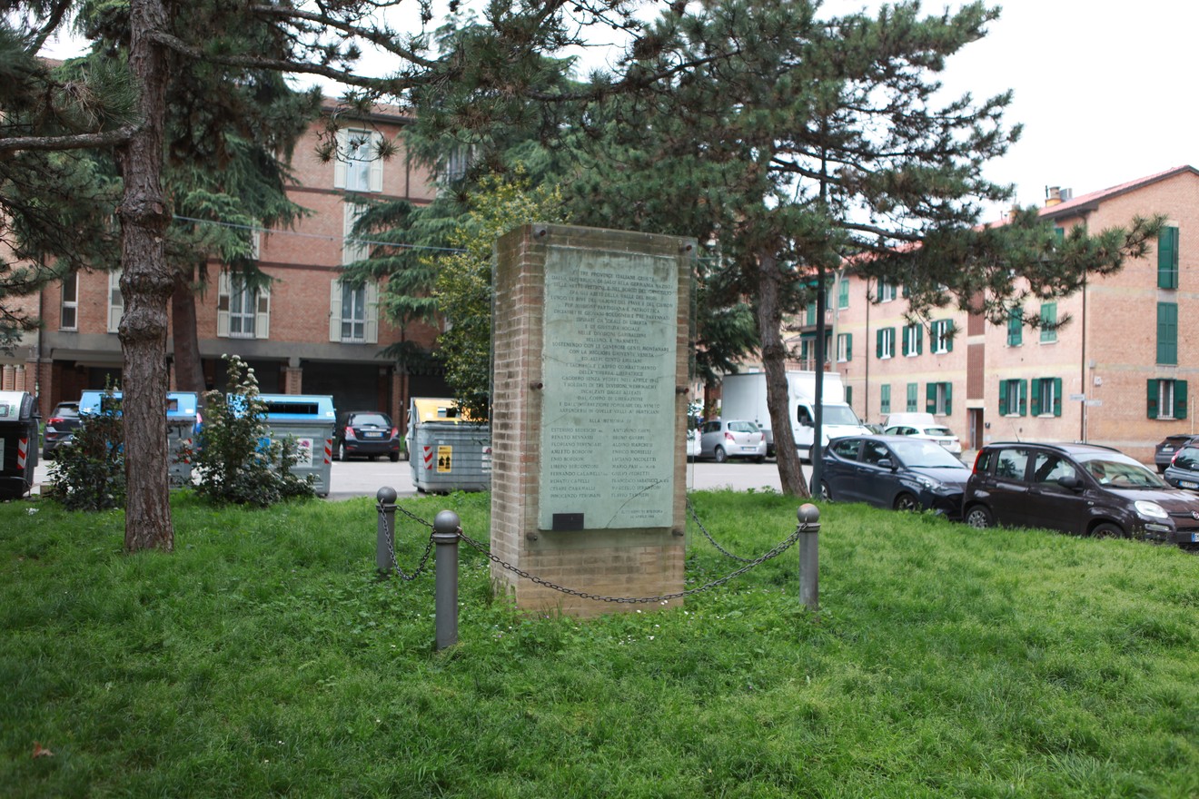 Monumento ai partigiani emiliani e romagnoli, circondato da alberi e veicoli in un contesto urbano.