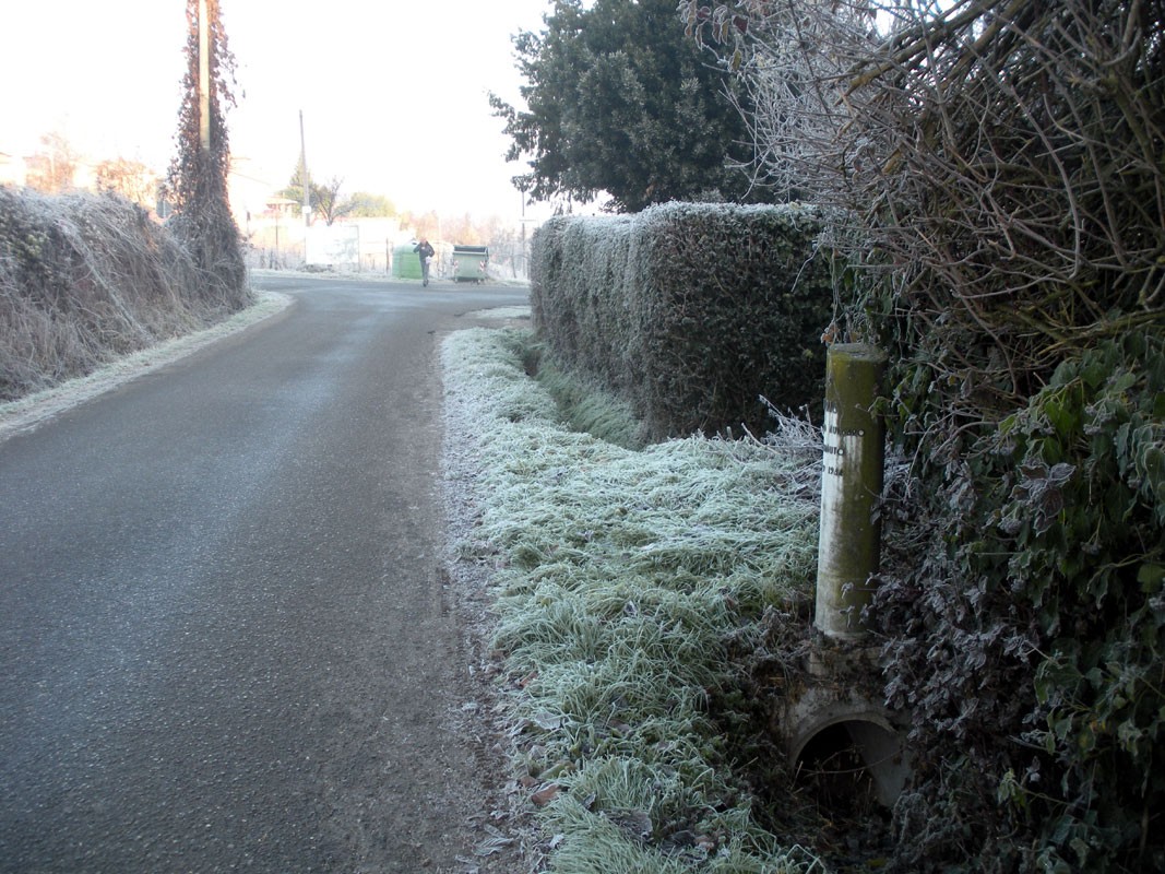 Cippo a Yoberdoff lungo una strada invernale, circondato da vegetazione ghiacciata.