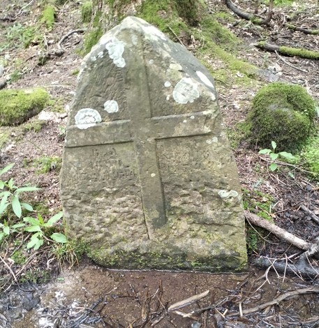 Cippo funerario in pietra con croce, immerso nella natura, simbolo di memoria e rispetto.