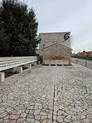 Monumento in memoria dell'eccidio di Villamarzana, circondato da un'area pavimentata e vegetazione.