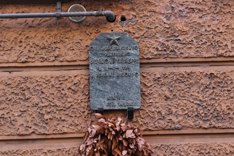Lapide commemorativa a Biscuola, affissa su una parete in pietra, con decorazioni di foglie secche.