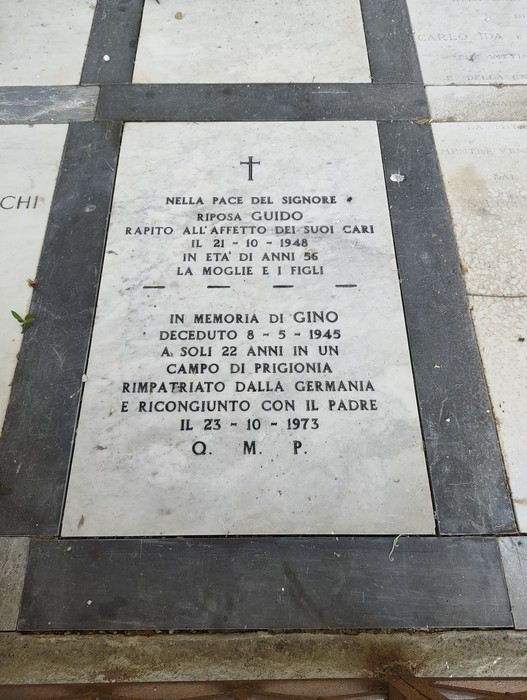 Lastra tombale in marmo bianco a terra, con croce incisa e iscrizione dedicata a due caduti.