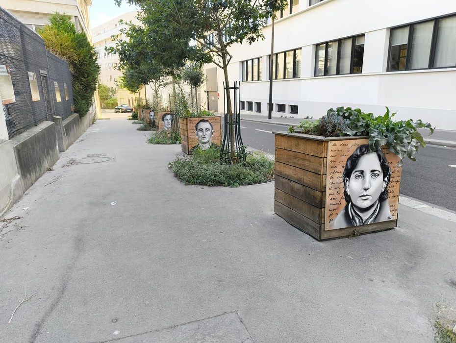 Targhe commemorative del Gruppo Manouchian su fioriere in una strada, con ritratti e messaggi di memoria.