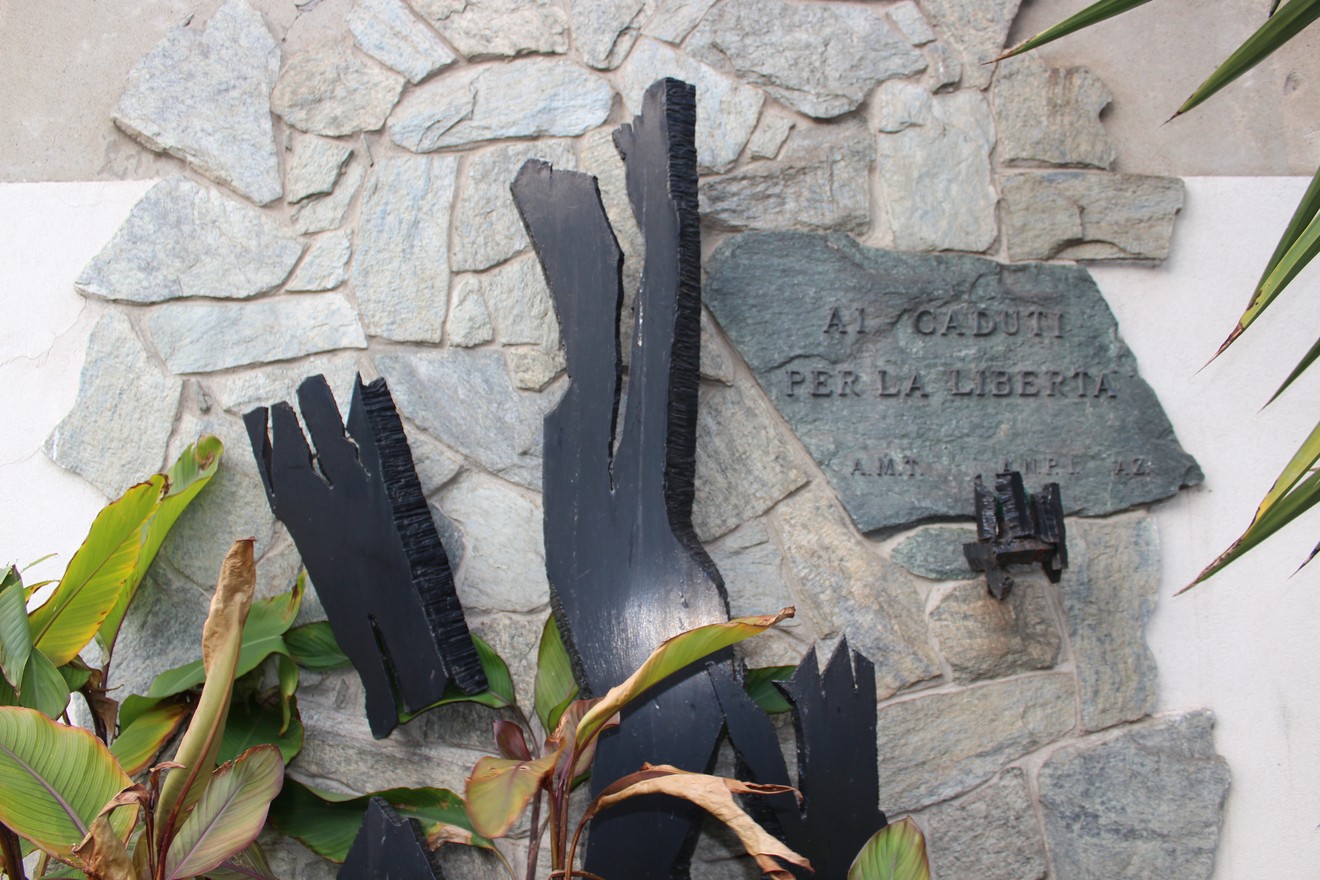 Monumento ai caduti per la Libertà, con elementi in pietra e legno scuro, circondato da piante verdi.
