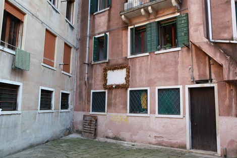 Una parete di un edificio in un vicolo, decorata con una cornice di rami secchi e un'area vuota centrale.