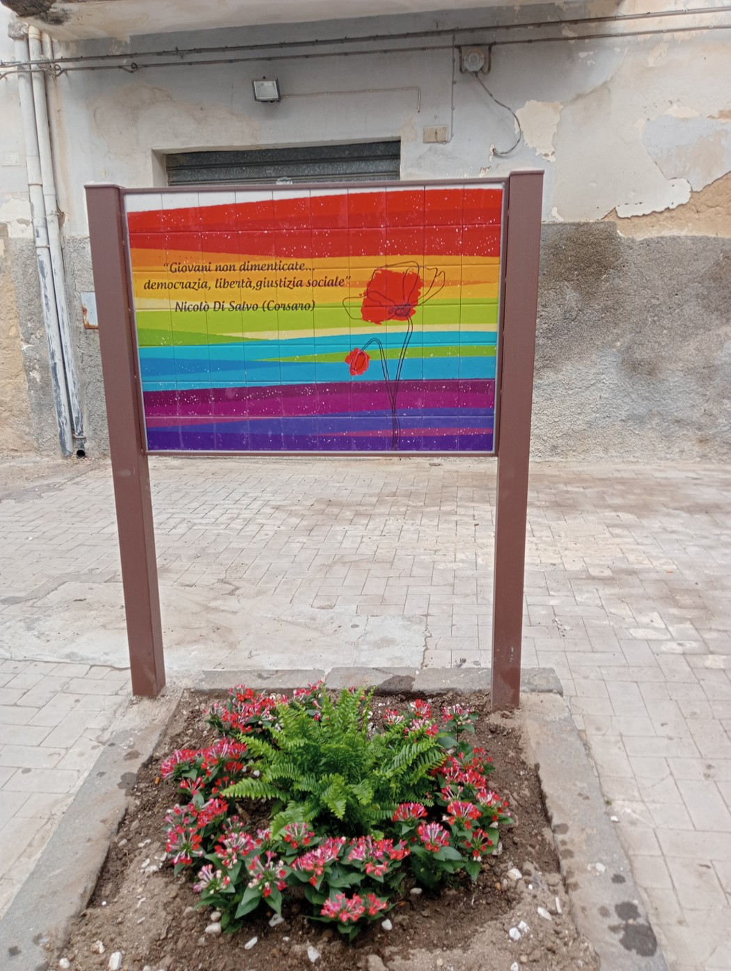 Lapide commemorativa dedicata a Nicola Di Salvo, decorata con fiori e colori vivaci.